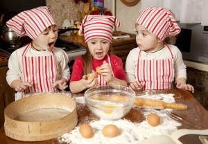 Three little chefs enjoying in the kitchen making big mess. Little girls making bread in the kitchen